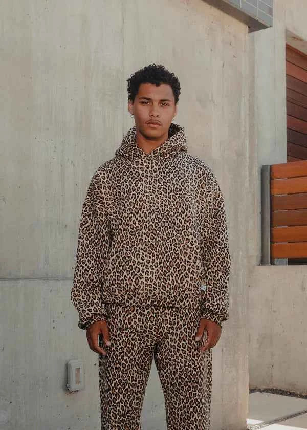 Person wearing a leopard print hoodie and pants standing against a concrete wall.